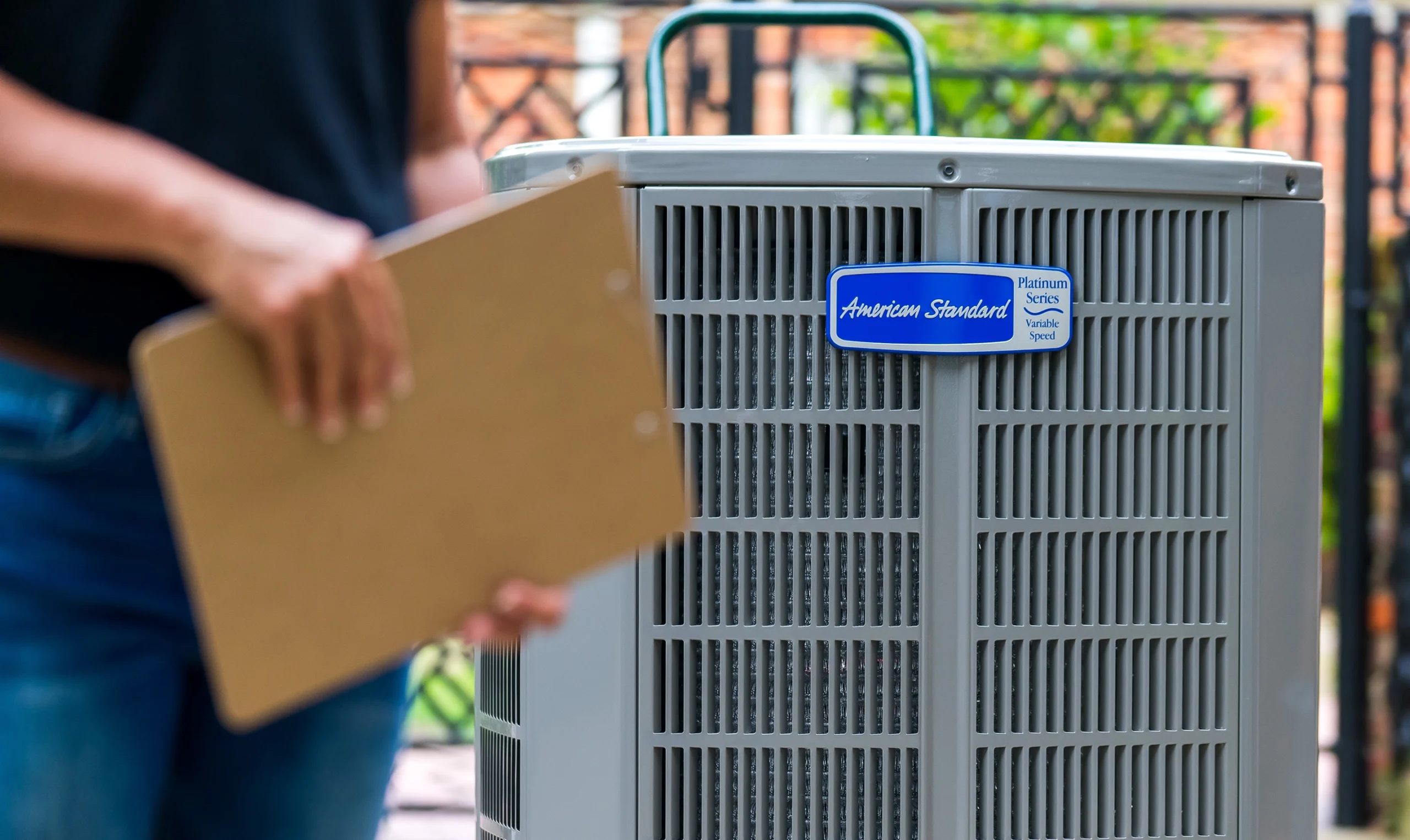 A closeup of an HVAC tech with a clipboard in front of an American Standard HVAC unit