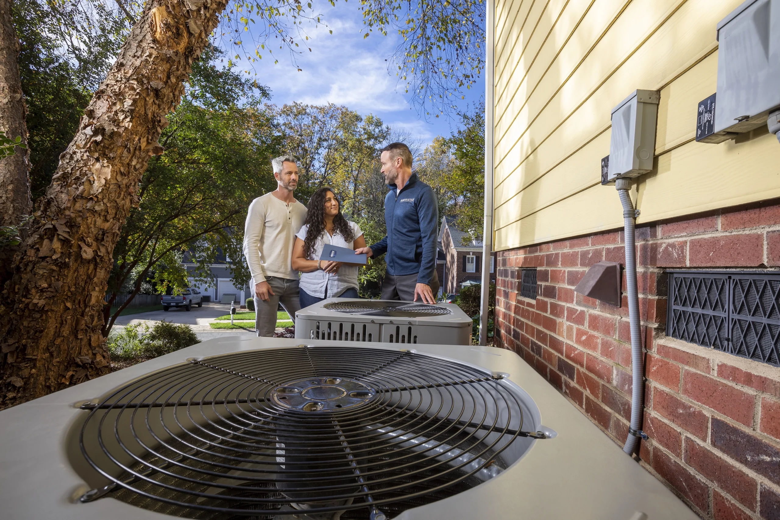 A couple speaks with an HVAC tech with two units in the forground